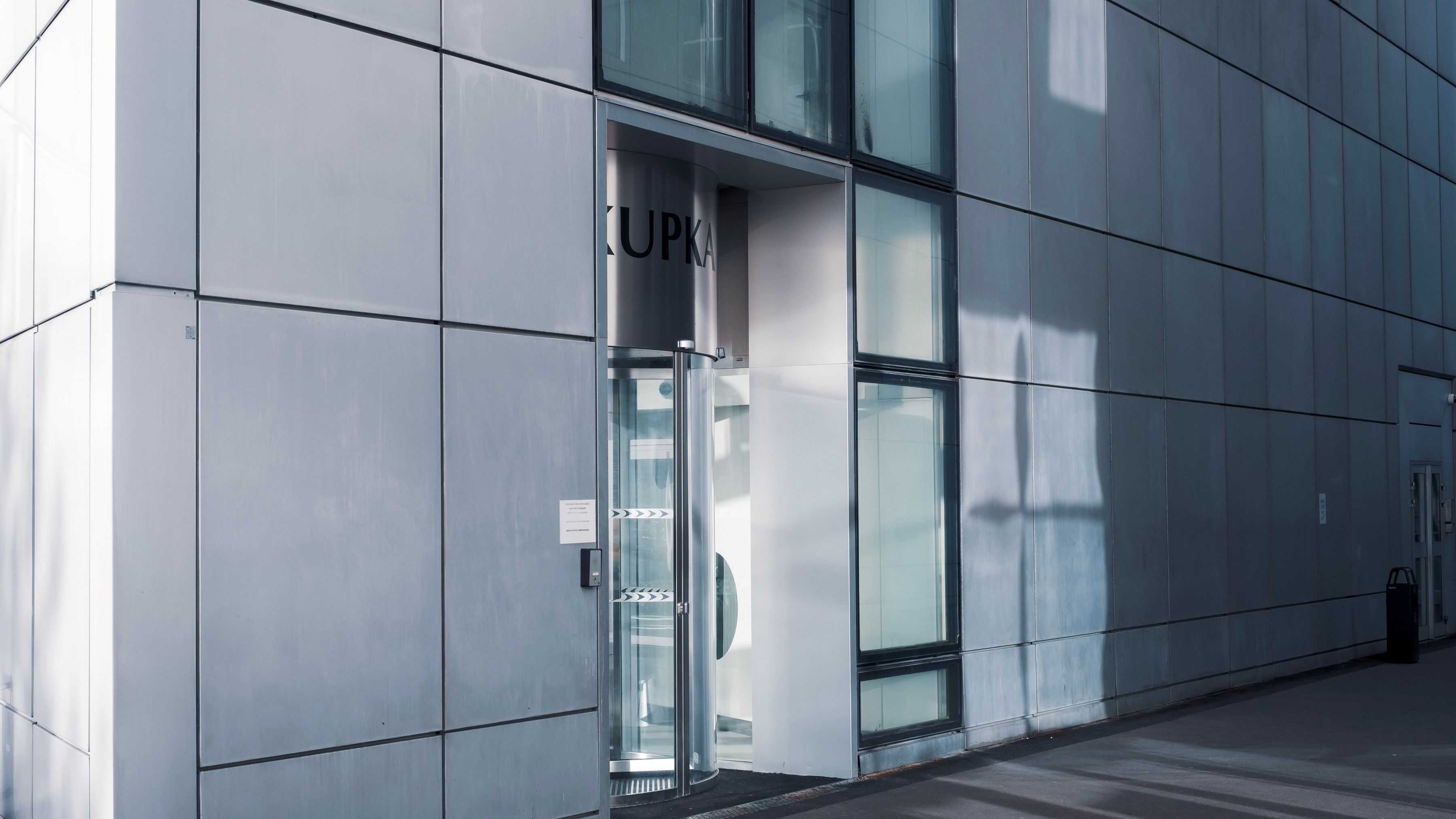 A modern office entrance with a single glass revolving door set into a pale paneled facade.